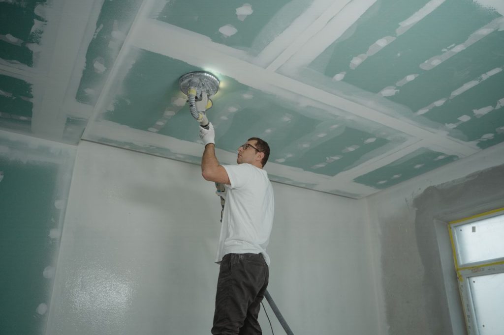A worker expertly polishes a ceiling indoors, demonstrating home renovation skills.